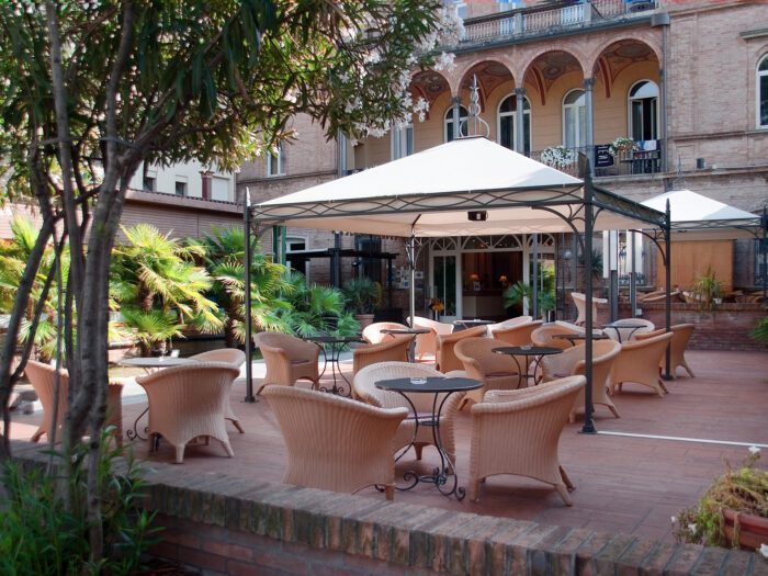 Der Unosider Novecento Pavillon vor einem Hotel im Innenhof mit diversen Gartentischen und Stühlen bei Tag