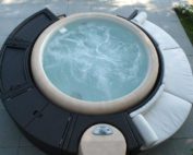 Dunkle Polyrattan Umrandung mit weisser Lounge zum Sitzen. Die Umrandung umrandet einen hellen sprudelden Softub Whirlpool.