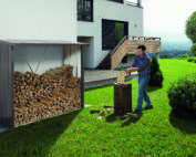 Man am Holzhacken im Garten vor einem dunkelgrauen Brennholzlager