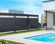 Biohort Sichtschutz in dunkelgrau metallic mit einem Acrylglas oben eingebaut. Der Sichtschutz steht in einem Garten vor einem Pool.