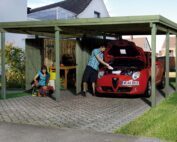 Weka Doppelcarport in grüner Farbe. Aus Holz. Mann steht vor einem roten alpha romeo. Links steht eine Abstellkammer