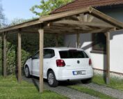 Massivholzdach Carport aus Holz im Garten mit einem weissen darunter parkierten Auto.