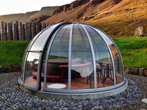 Abgebildet ist der Softub Spa Dome, der einen Softub Whirlpool überdeckt. Beides steht in einem Garten auf einem Steinboden.