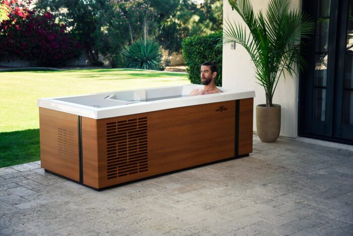 Rectangular brown icebath on a patio in a garden. A man is bathing in the icea bath