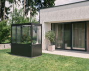 Dunkelgraues Metall Gewächshaus mit Pflanzen vor Architektenhaus im Garten