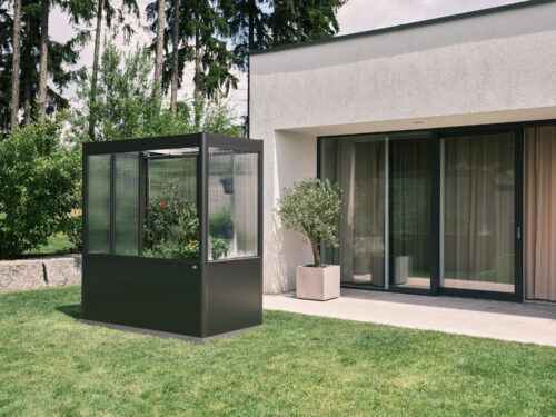 Dunkelgraues Metall Gewächshaus mit Pflanzen vor Architektenhaus im Garten