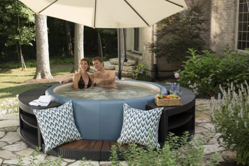 A couple is enjoying the Softub Legend hot tub with a polyrattan frame and step entry. The Softub is under a parasol on a terrace.
