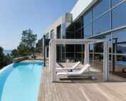 Ein weisser Pavillons mit zwei weissen Sonnenliegen auf einer grossen hölzerner Terrasse mit Pool
