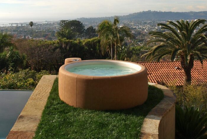 Heller runder Whirlpool auf einer Terrasse mit Pool und Ausblick auf eine Stadt am Meer