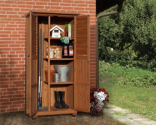 narrow wooden equipment cabinet on a red brick wall next to a lawn. Cabinet is filled with different garden tools and utensils.