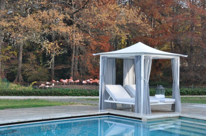 Unosider Pavillon Day Living vor einem Pool in einem grossen Garten. Unter den Pavillons stehen jeweils zwei Liegen.