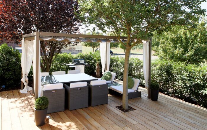 Unosider Pavillon Mood mit weissen, zusammengebundenen Vorhängen auf einer Terrasse mit Holzboden in einem Garten