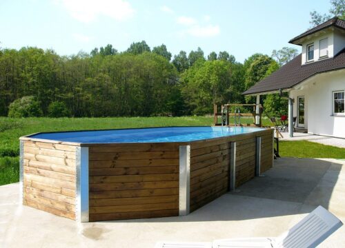 Basic solid wood pool from Weka. Large, angular swimming pool in natural wooden look. Stands in front of a large, white house.