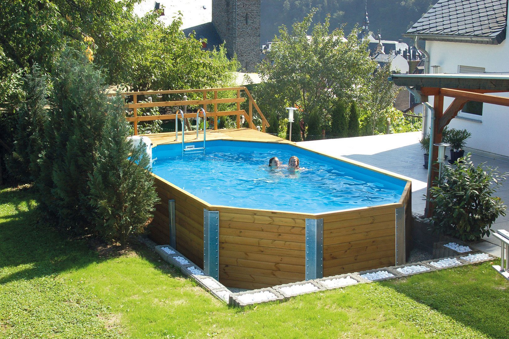 Massivholzpool von Weka. Grosser Weka Swimmingpool im Garten vor einem weissen Haus. Der Pool ist gefüllt mit zwei Kindern.