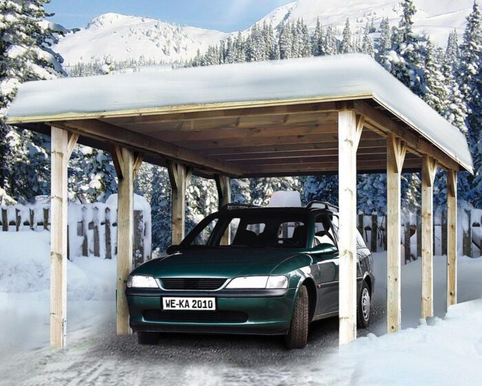 Holzcarport mit vier Balken auf jeder Seite. Schneebedeckt in den Bergen. Grünes Auto unter dem Carport geparkt.