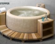Runde, helle Holz Umrandung mit Regalen und einem Treppentritt für einen hellen, runden Whirlpool. Newport Softub Stepper aus Holz