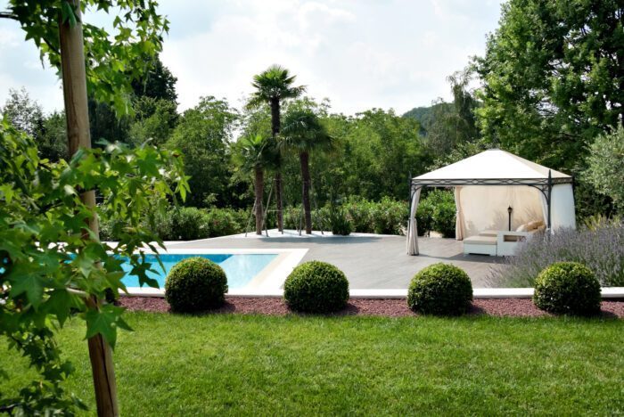Weisser Unosider Pavillon Novecento spendet Schatten einer weissen Gartenlounge vor einem Pool.
