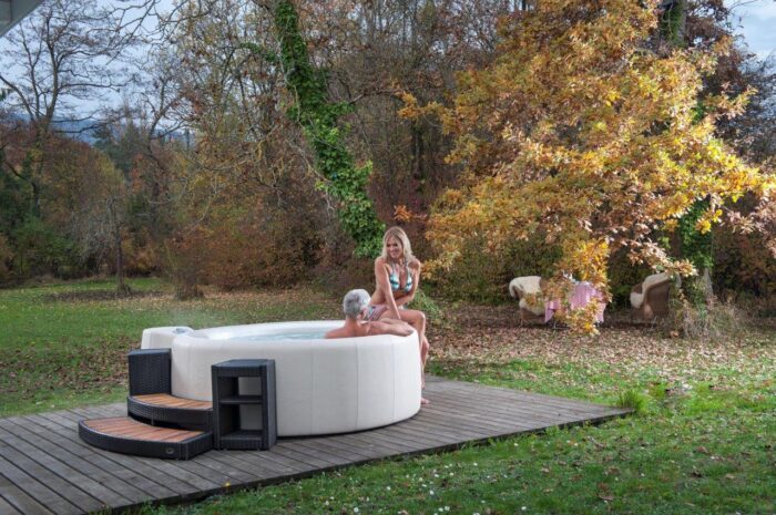 The Softub Whirlpool Resort in off-white with polyrattan and Holystair entry, in a garden with colourful trees.