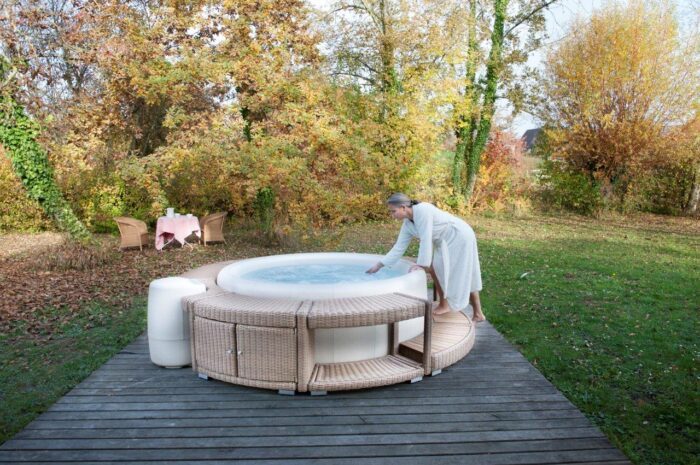 Softub whirlpool resort in almond with a brown polyrattan surround on a terrace and garden with colourful trees.