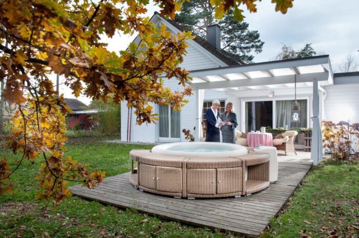 Softub Resort in off-white mit einer braunen Polyrattan Umrandung auf einer Terrasse vor einem grossen, weissen Haus.