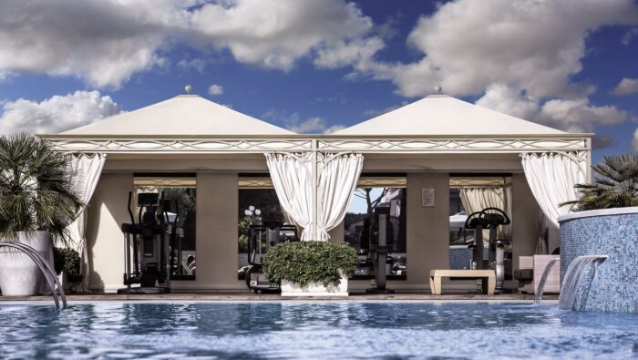 Zwei Unosider Pavillon Novecento Rain vor einem grossen Pool mit weissen Vorhängen und einem spitzen Dach.