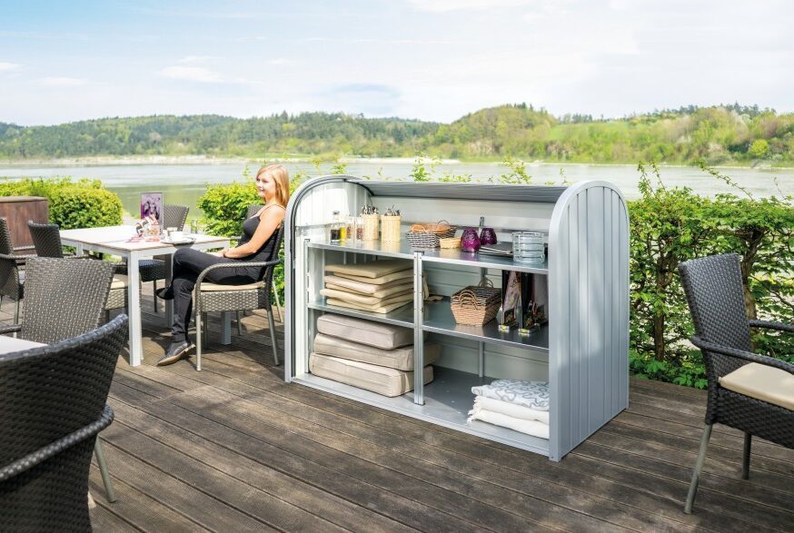 Gartenbox in silber mit abgerundeten Ecken in silber. Die Gartenbox steht auf einer Terrasse eines Restaurants vor einem See. Die Box ist geöffnet.