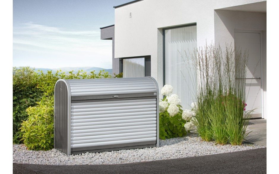 Gartenbox mit silber und quarzgrauen Grautönen. Die Gartenbox mit abgerundeten Ecken steht vor einem grossen weissen Haus mit grossen Ganzglasfenstern