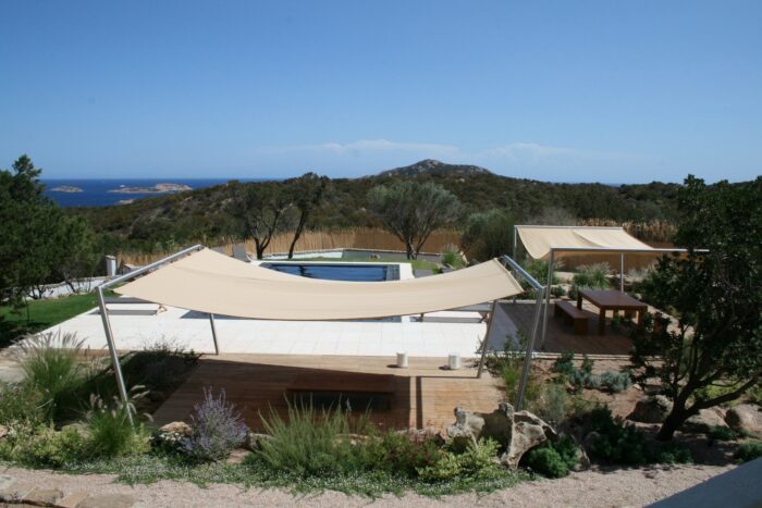 Unosider Sonnensegel Carloforte bietet Schatten über einer Terrassenlounge neben einem Pool mit Aufsicht aufs Meer.