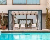 Der Unosider Pavillon Mood YPE vor einer grossen Villa mit Pool mit weissen Liegestühlen, Vorhängen und Dach