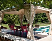 Unosider Pavillon Novecento spendet Schatten an eine rote Gartenlounge vor einem Pool