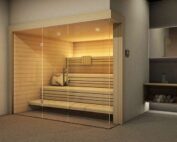 Sauna aus hellem Holz mit hellen Bänken. Innendurch beleuchtet mit indirekter Beleuchtung und Ganzglasfront.