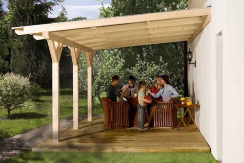 A natural terrace canopy with three posts. The canopy leans against a white wall of a house and stands on a wooden surface. Underneath the canopy a family with kids is sitting on dark brown garden chairs at a dark brown garden table